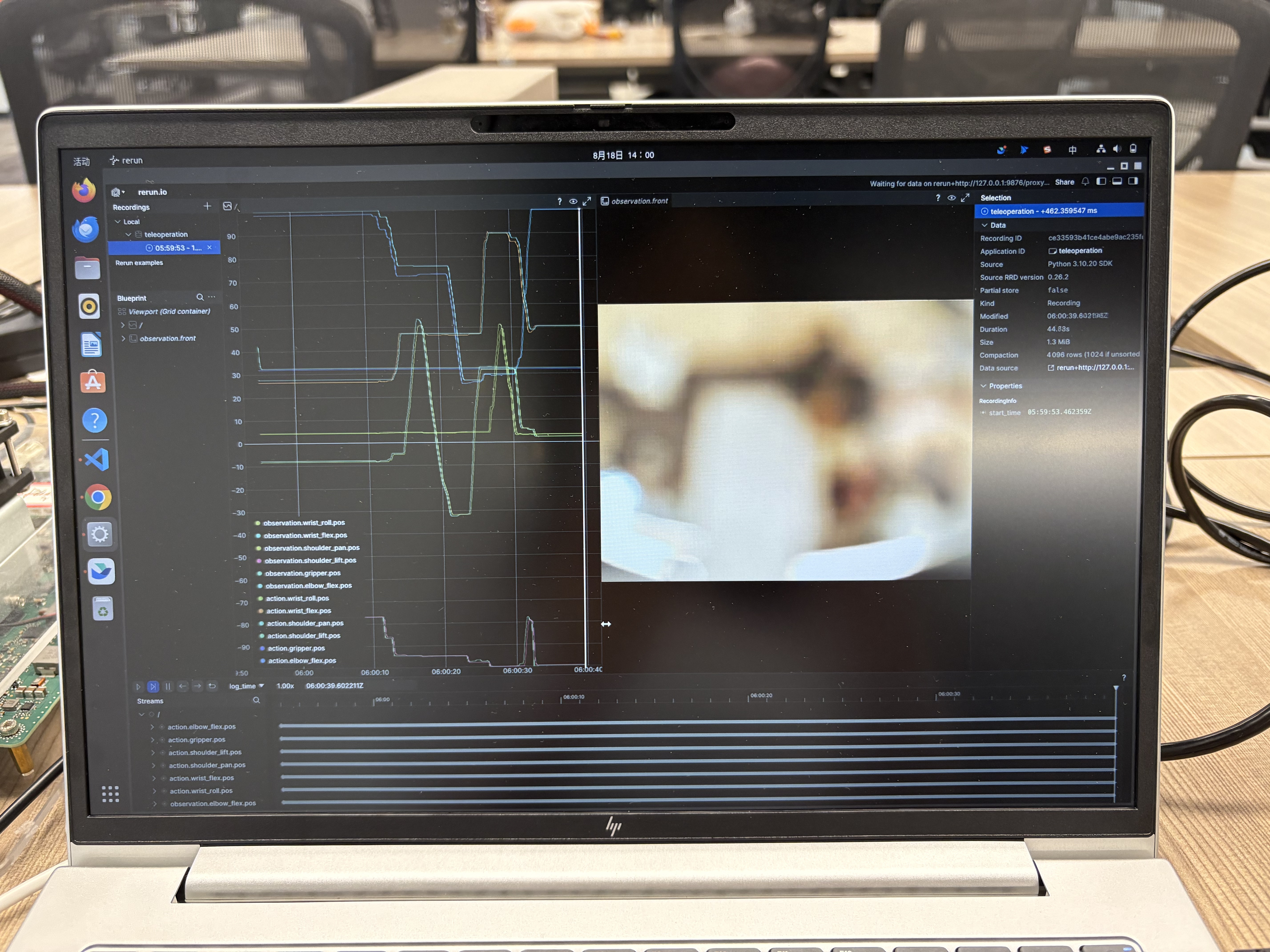 A laptop at the project workspace displaying teleoperation joint curves and a front camera view in Rerun